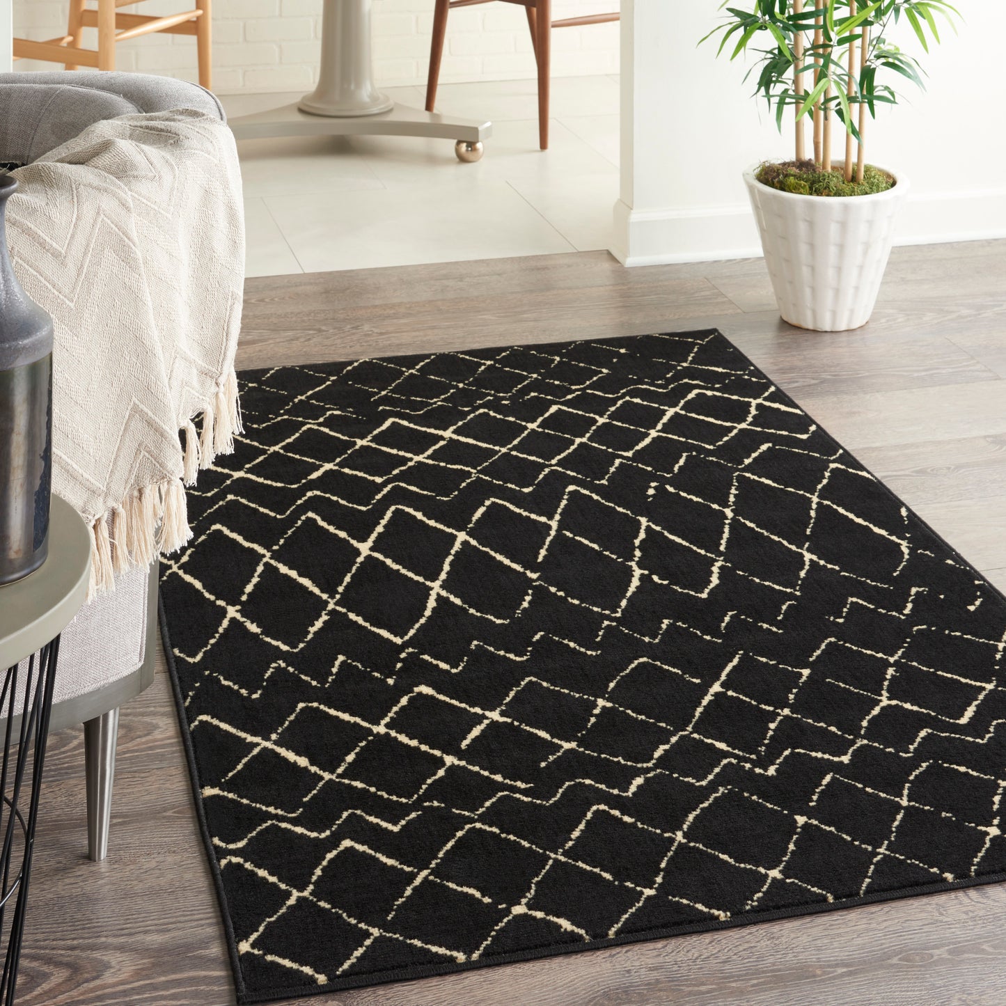 Black rug with white geometric lattice pattern on wood floor, living room with plant and beige throw.