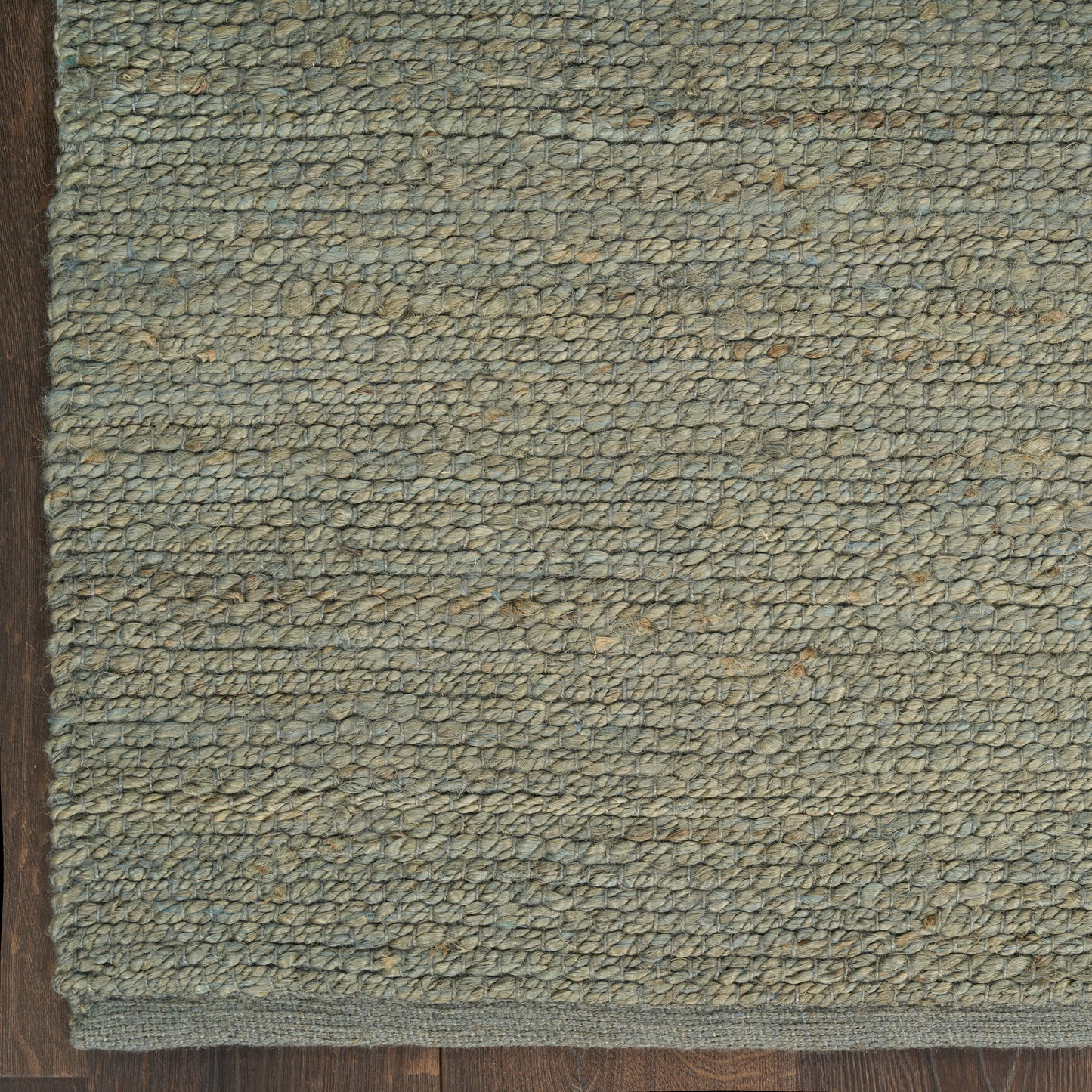 Blue-gray looped-pile rug with beige flecks and dark brown border on wood floor.