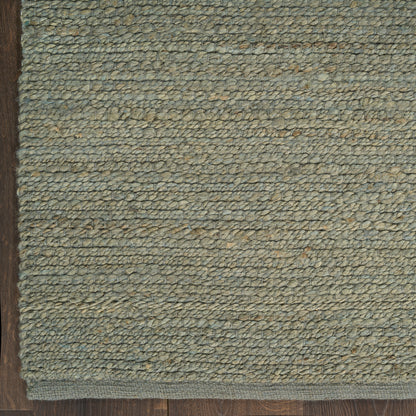 Blue-gray looped-pile rug with beige flecks and dark brown border on wood floor.