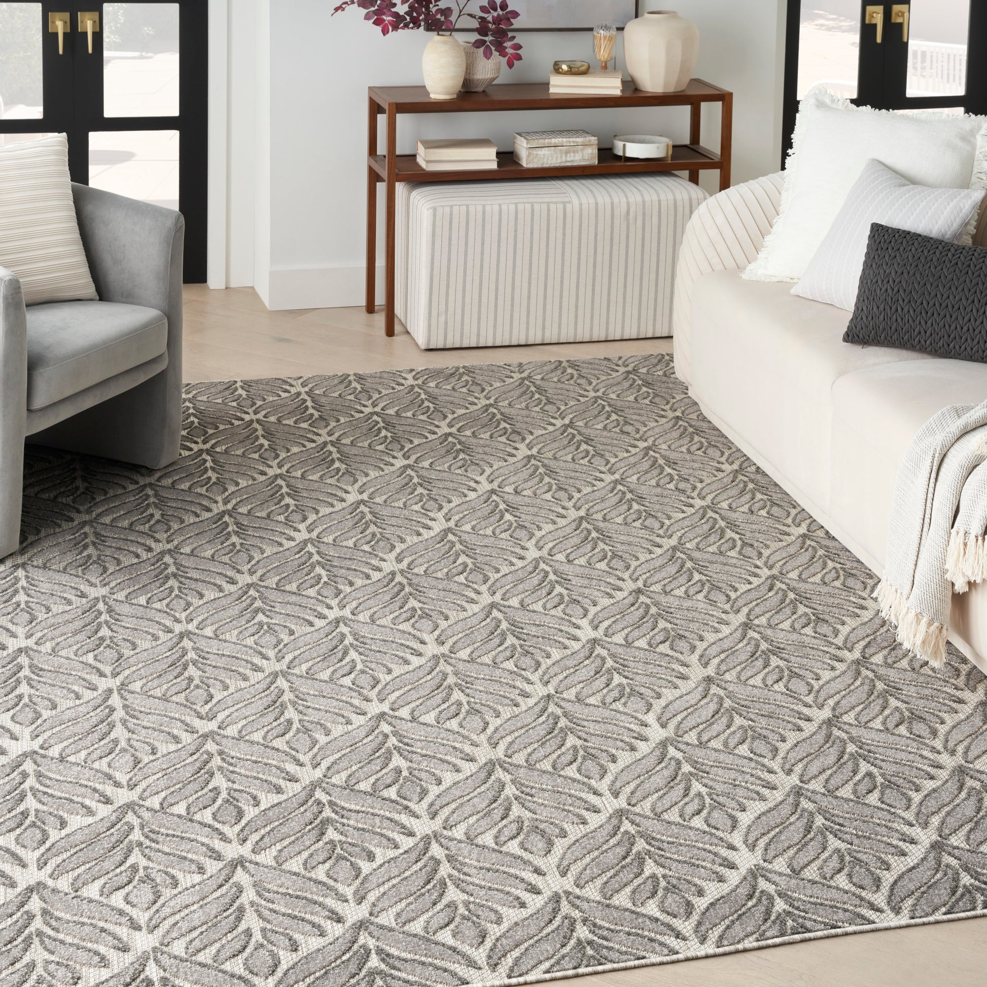 Textured gray and beige area rug with leaf-shaped pattern in a modern living room with a neutral sofa and armchair.