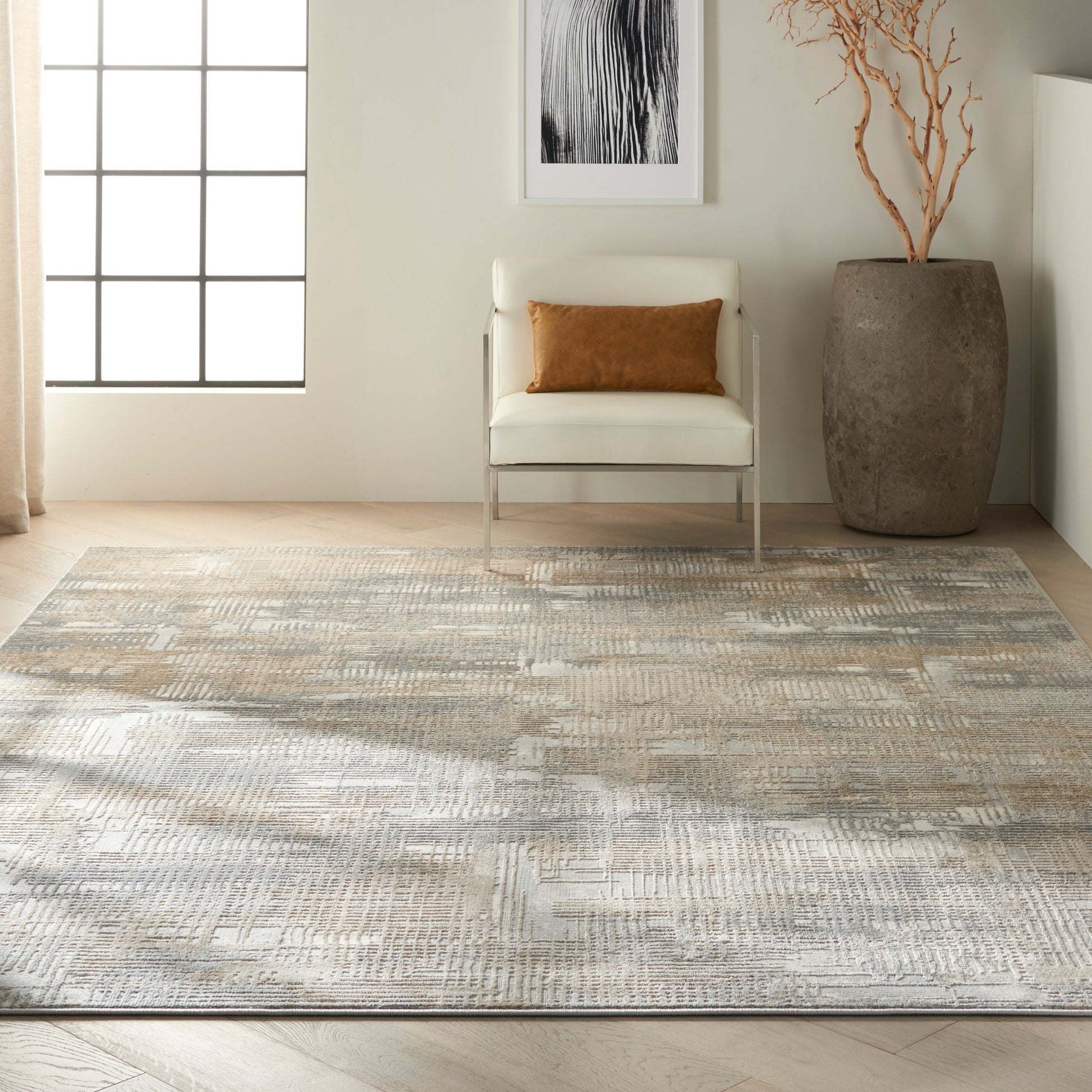 Neutral beige-gray geometric area rug with white modern armchair, brown pillow, tall ceramic vase and dried branches.
