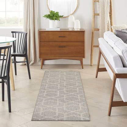 Long grey geometric rug runner in a sunlit living room with walnut dresser, round glass table, black chairs, and a light sofa.