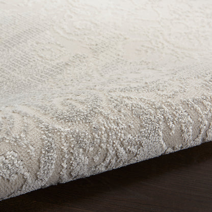 Beige damask-patterned area rug with plush textured pile on dark wood floor.
