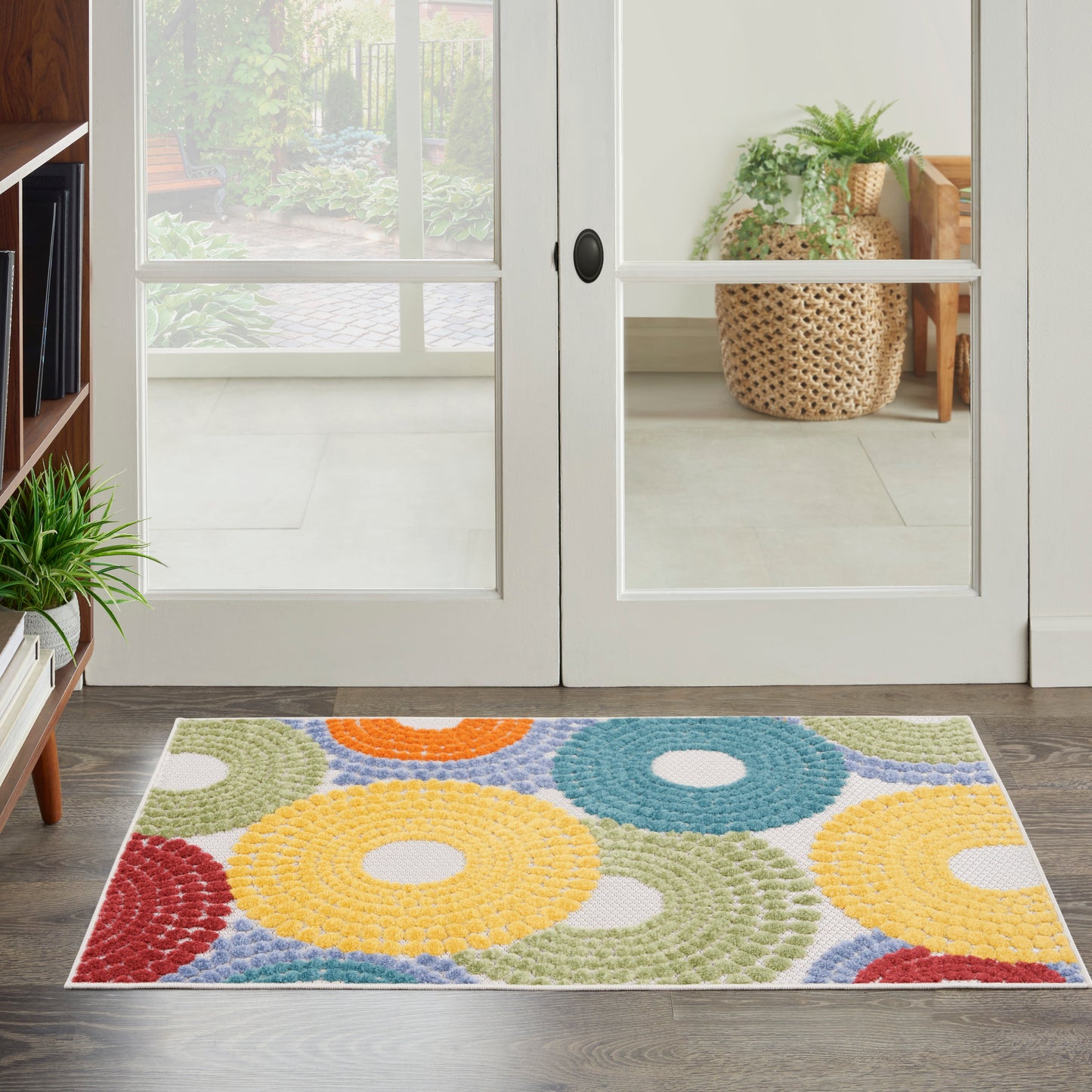 Multicolor rectangular rug with donut-shaped rings in yellow, blue, green, red and orange by glass doors.