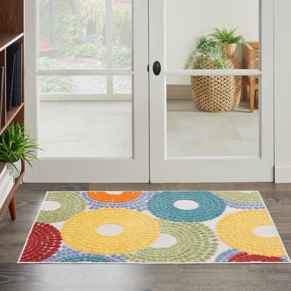 Multicolor rectangular rug with donut-shaped rings in yellow, blue, green, red and orange by glass doors.