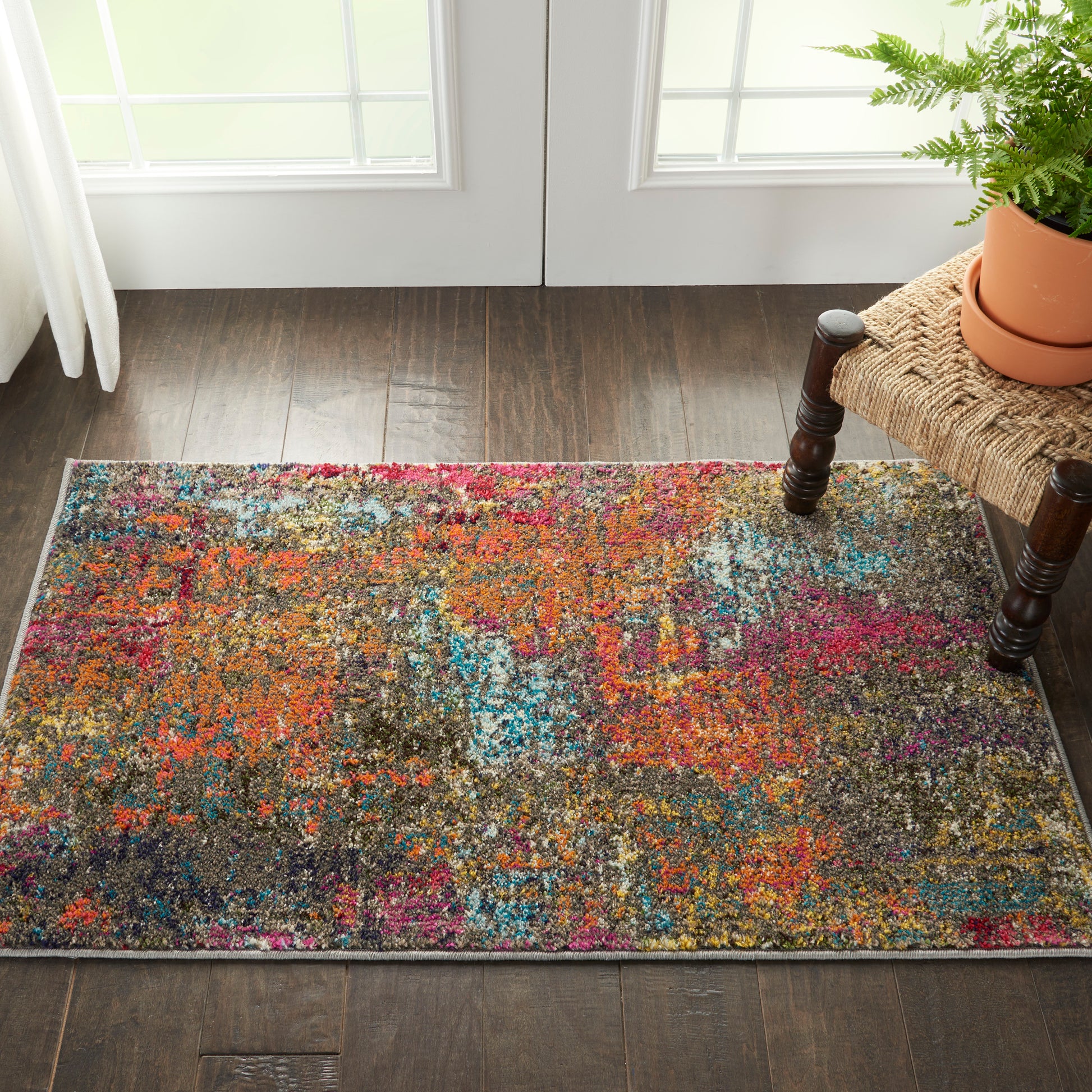 Colorful abstract shag rug in orange, pink, blue and purple hues on dark wood floor beside a woven bench with a fern.