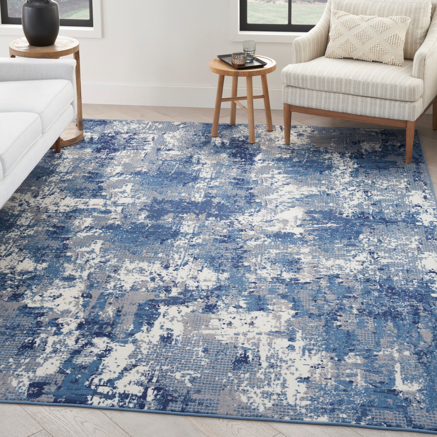 Blue and white abstract distressed area rug in a modern living room with a beige sofa and wooden tables.