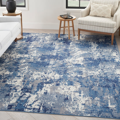 Blue and white abstract distressed area rug in a modern living room with a beige sofa and wooden tables.