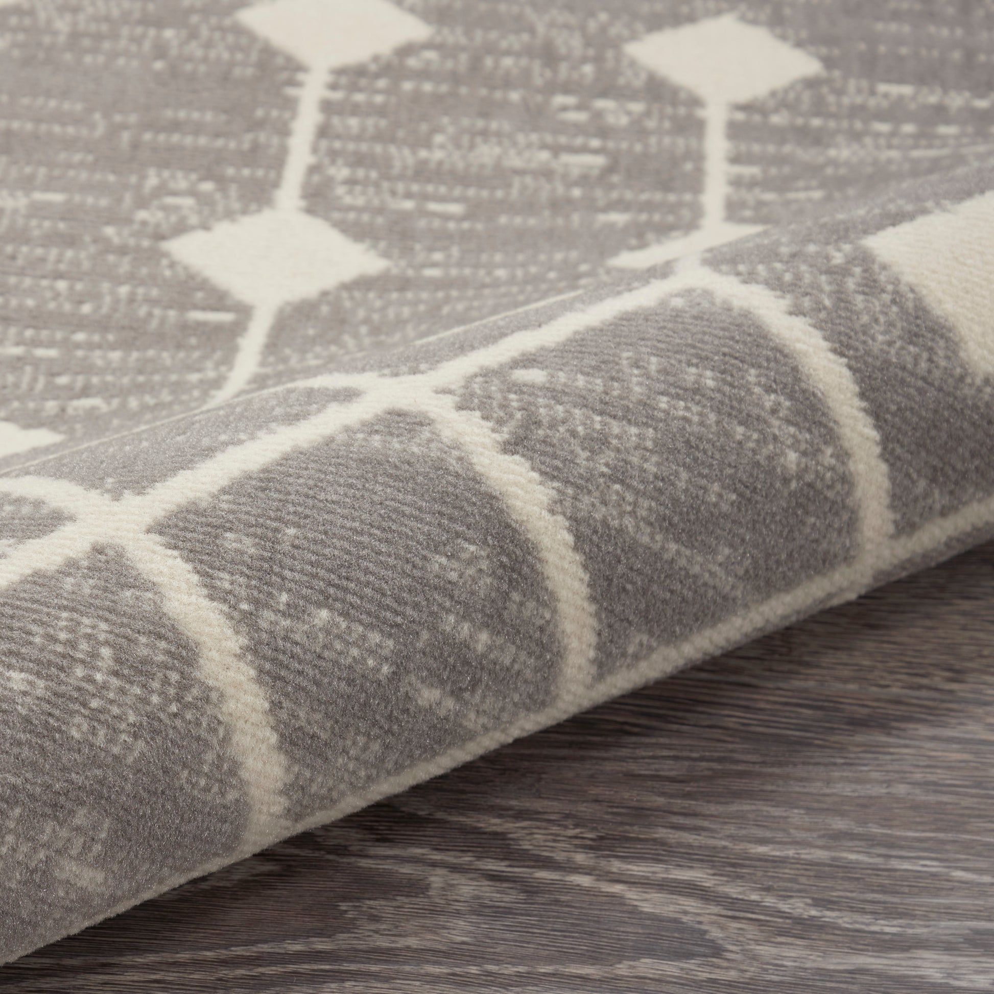 Gray and ivory geometric rug with diamond lattice pattern and woven texture, rolled edge on dark wood floor.