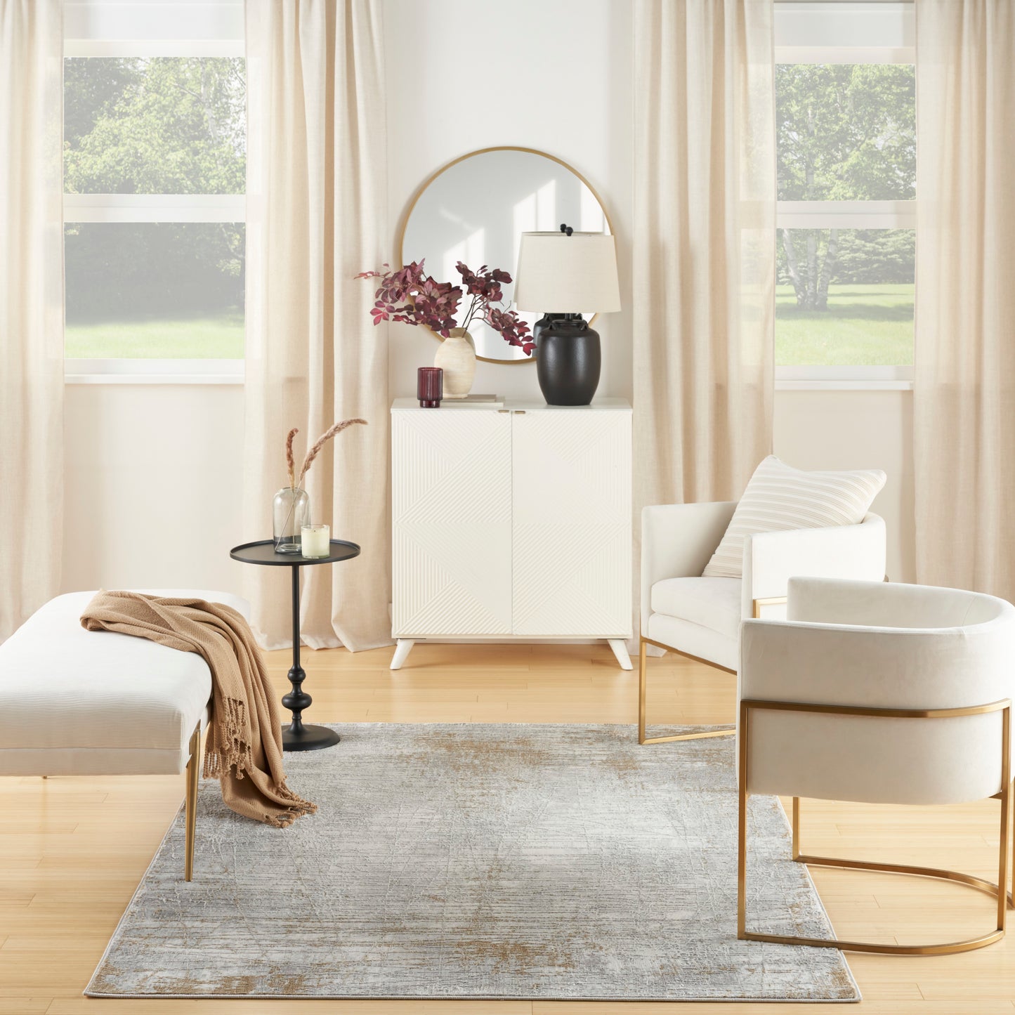 Neutral living room with white cabinet, round mirror, black lamp, pink flowers; beige curtains, cream chairs on gray rug.