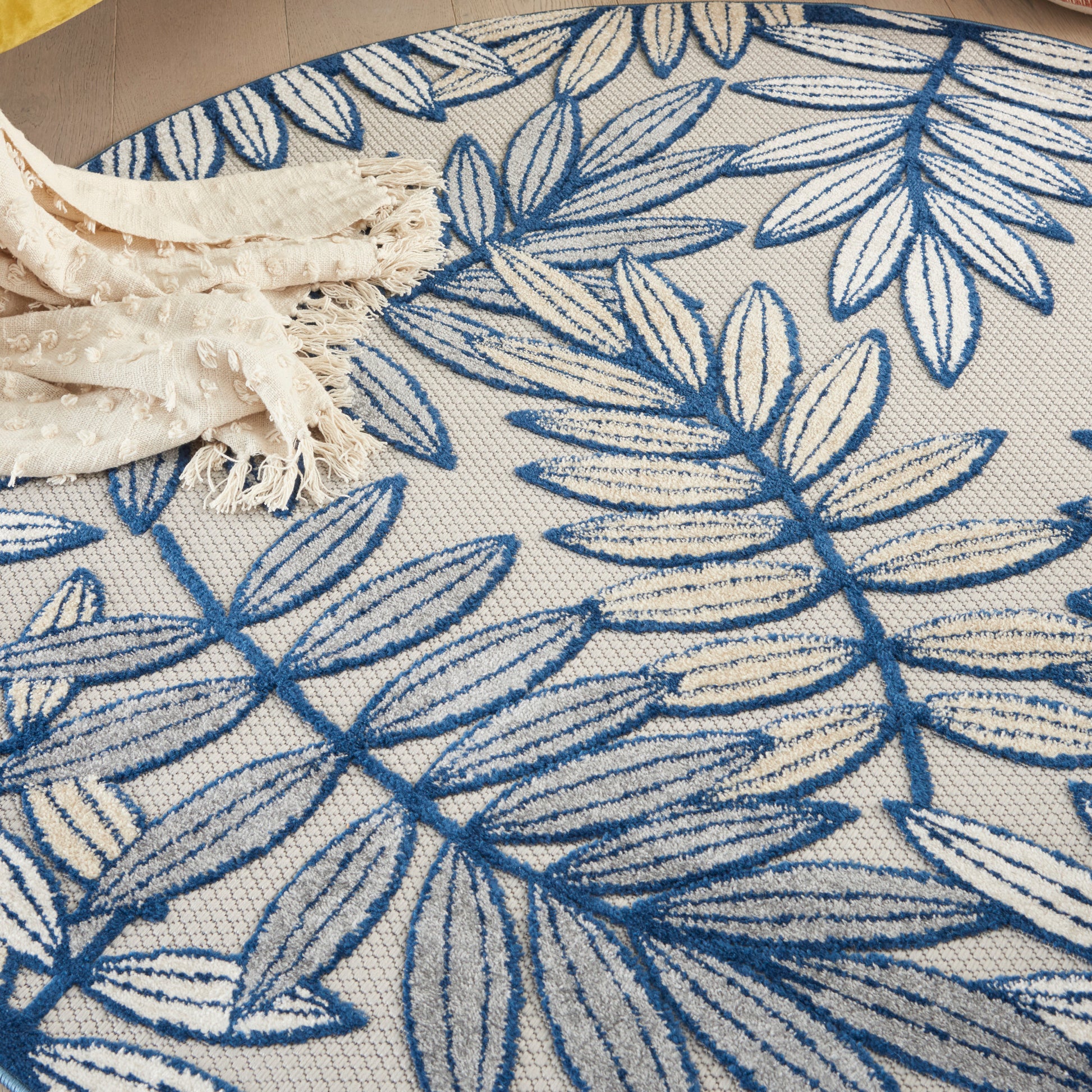 White rug with bold blue leaf pattern and a beige fringed throw resting on top.