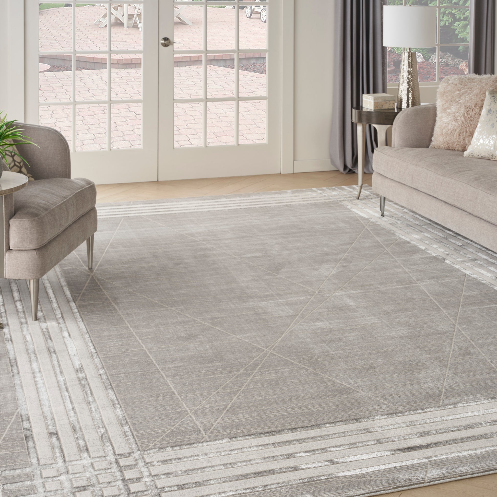 Soft gray geometric area rug with light border stripes in a modern living room, taupe sofa & armchair, glass French doors.