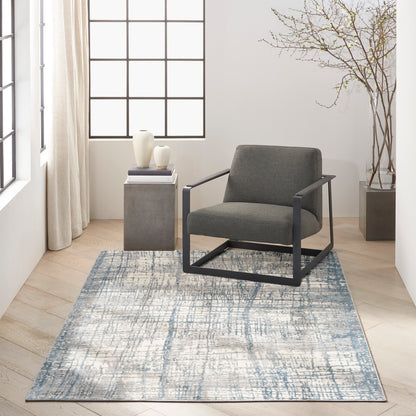 Blue abstract rug (5' x 7') beneath a modern seating area featuring a grey upholstered chair with a black metal frame and a concrete side table.