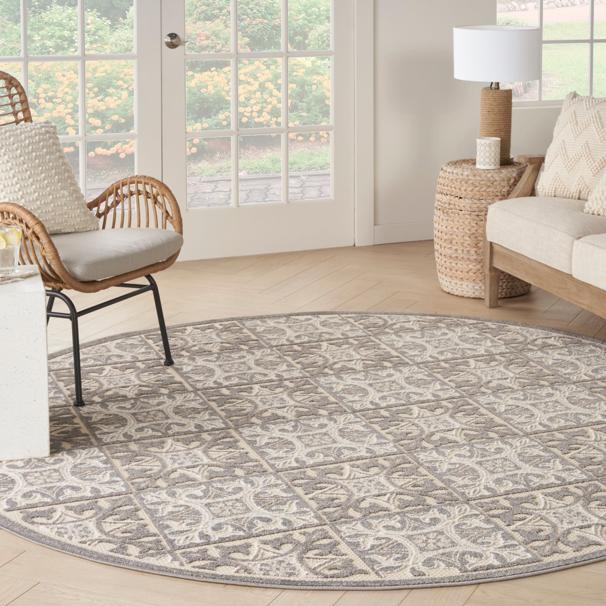 Round gray patterned rug in a bright living room with wicker chair, beige sofa, woven side table, and French doors.