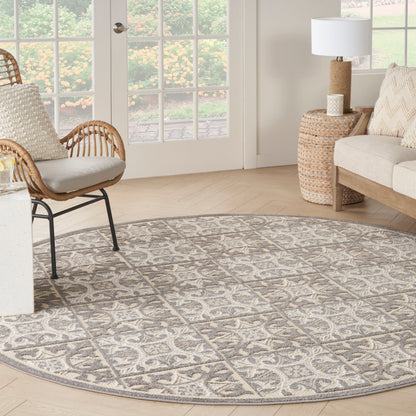 Round gray patterned rug in a bright living room with wicker chair, beige sofa, woven side table, and French doors.