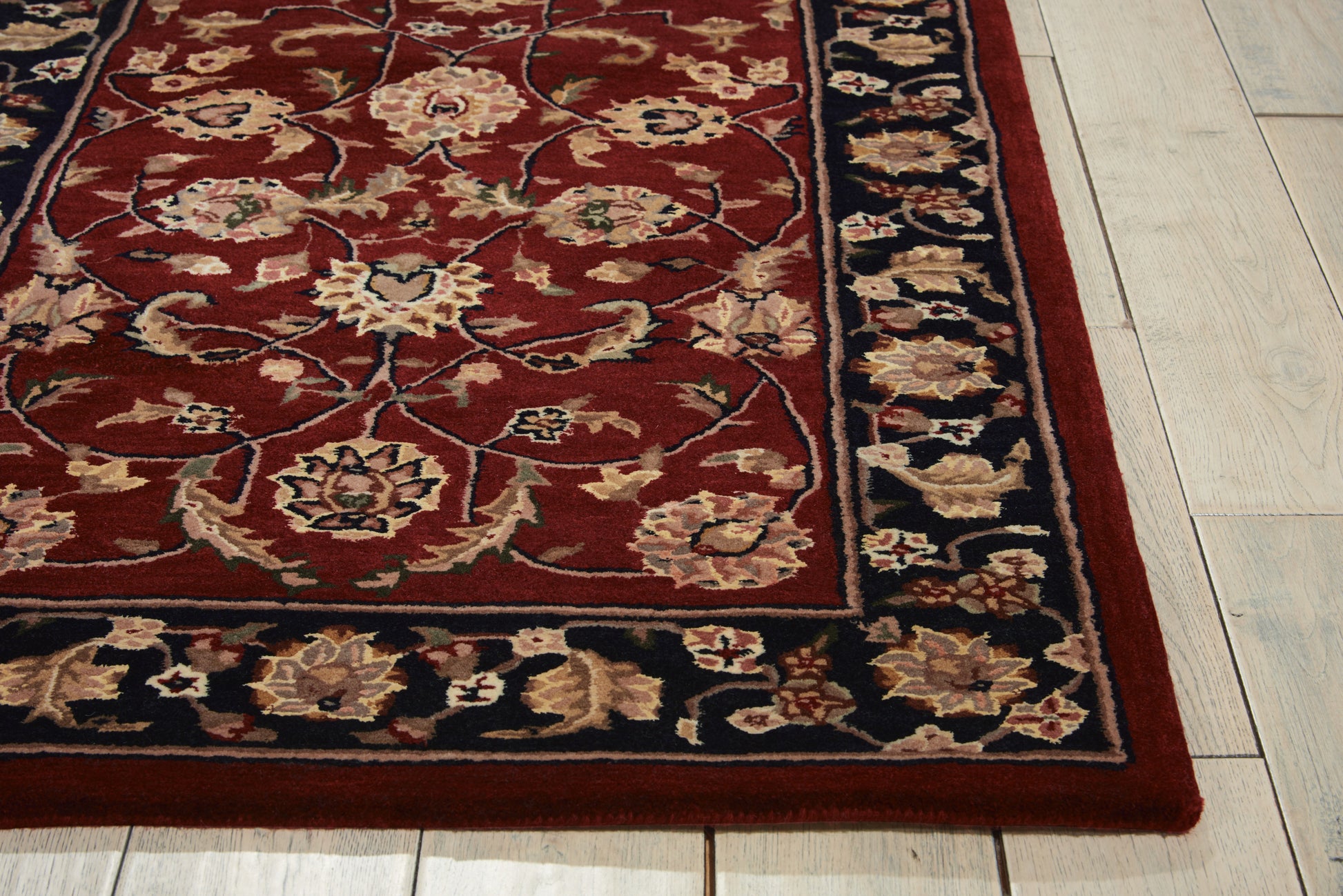 Rectangular oriental rug with deep red field, ivory floral motifs, dark blue border, on light wood floor.
