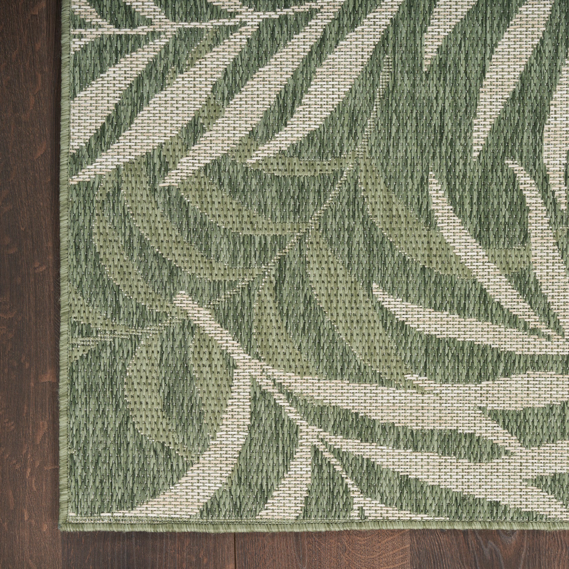 Rectangular woven rug with green botanical leaf pattern on dark wood floor.