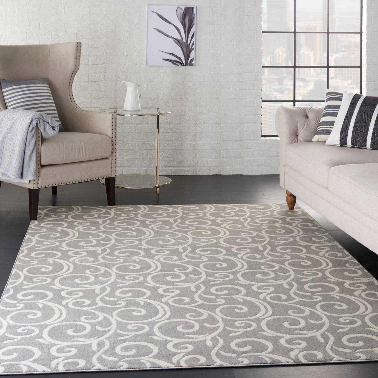 Gray-and-white swirl rug in a contemporary living room with neutral beige seating, glass side table, brick wall and city view.