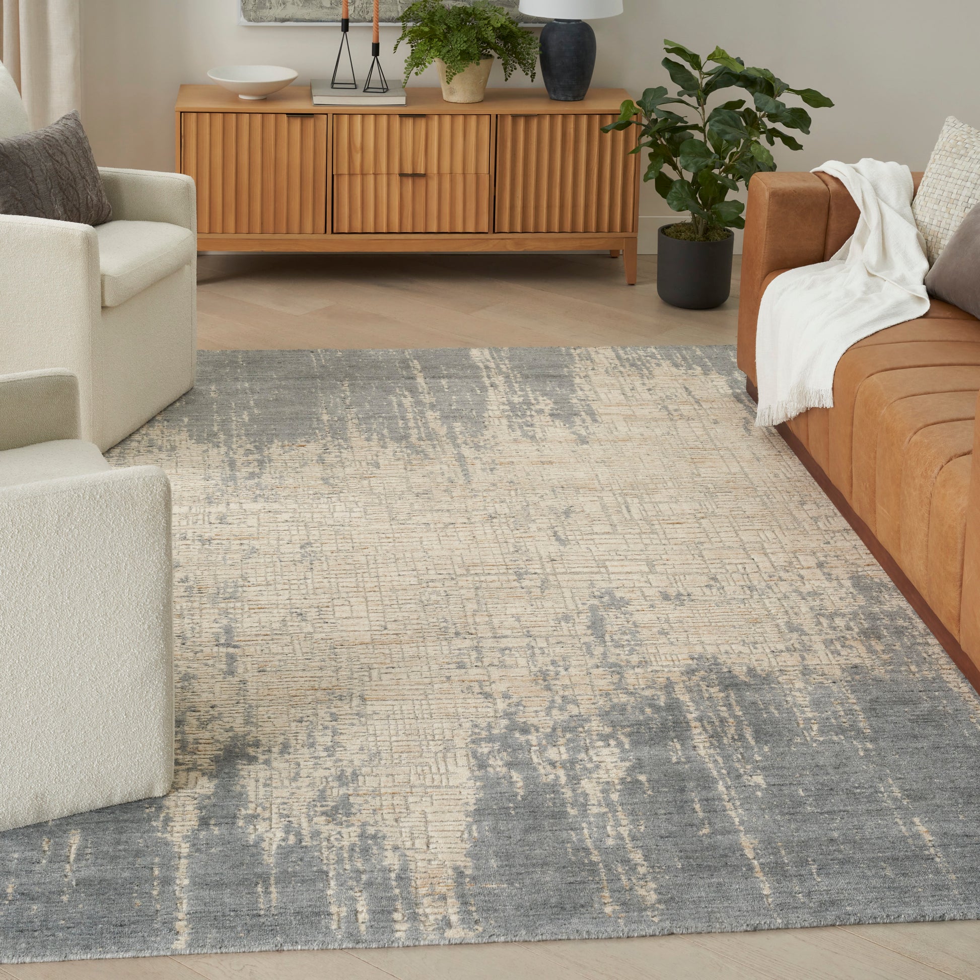 Distressed blue-beige area rug in a modern living room with tan sofa, cream chairs, wooden mid-century cabinet, and plants.