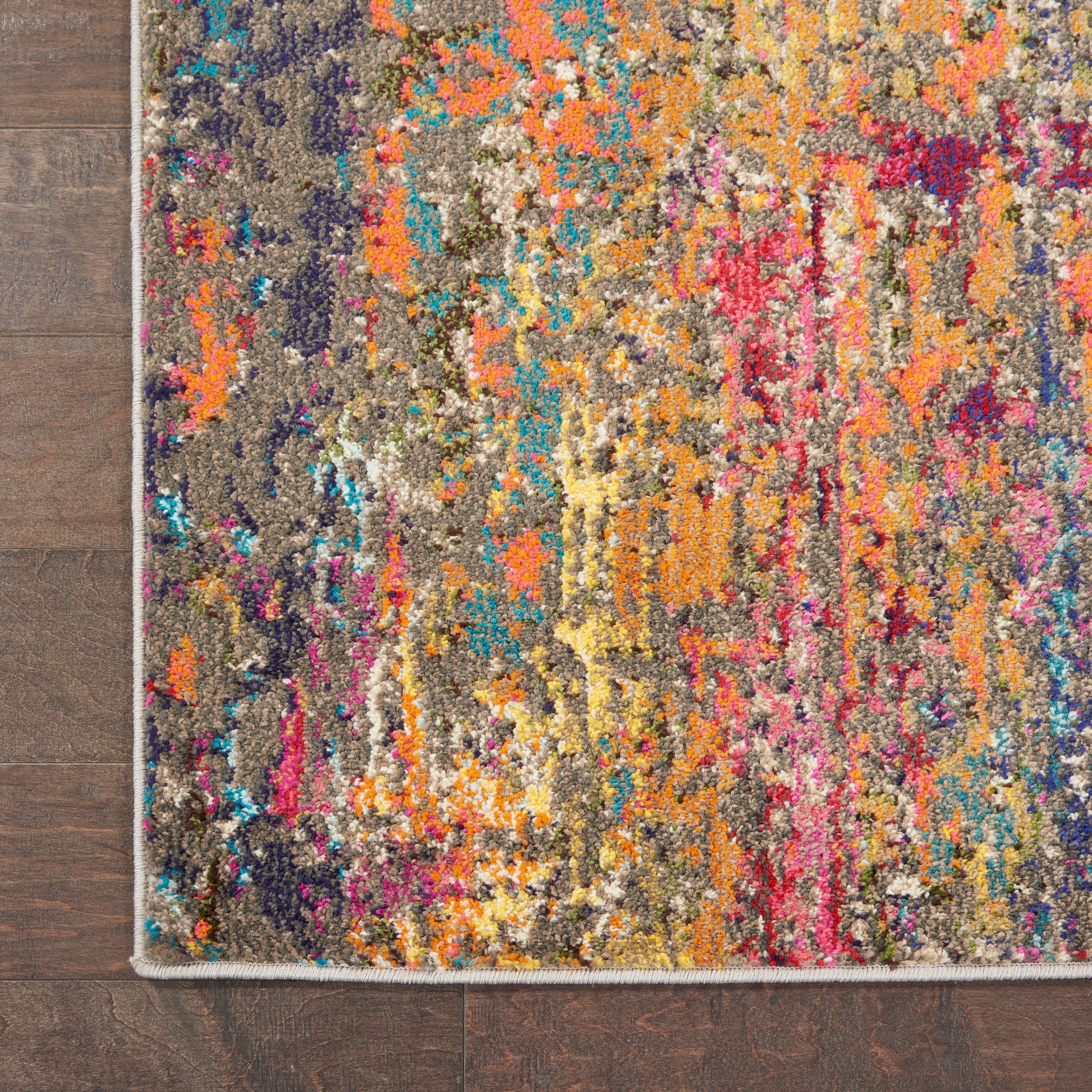 Rectangular multicolor abstract runner rug with orange, pink, teal and purple on a brown base; light fringe edge on a wooden floor.