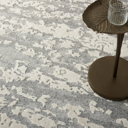 Grey and ivory abstract-pattern area rug with a bronze leaf-shaped side table and a glass votive on top.