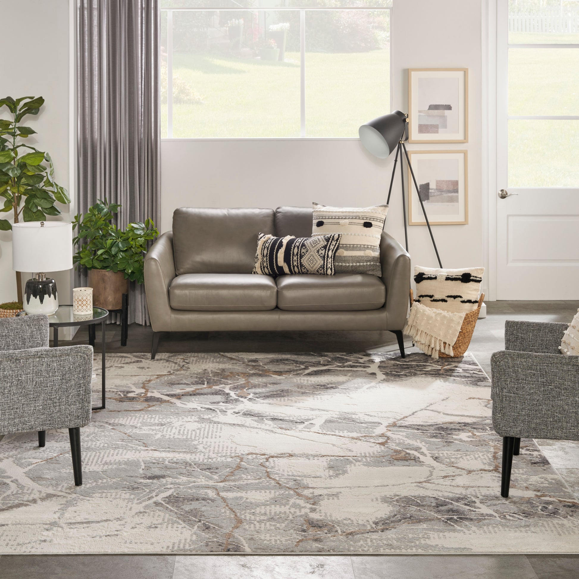 Gray leather sofa with patterned pillows in a bright living room; abstract rug, plants, tripod lamp, woven basket.