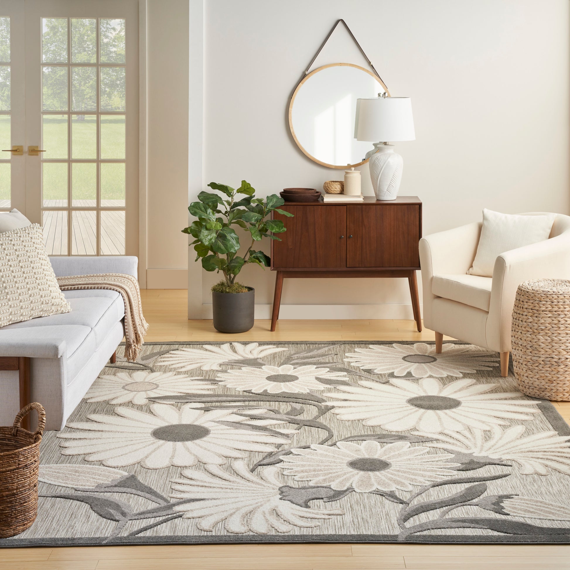 Living room with a large gray and ivory floral rug, mid-century wood sideboard, white chairs, and potted plant.