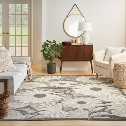 Living room with a large gray and ivory floral rug, mid-century wood sideboard, white chairs, and potted plant.