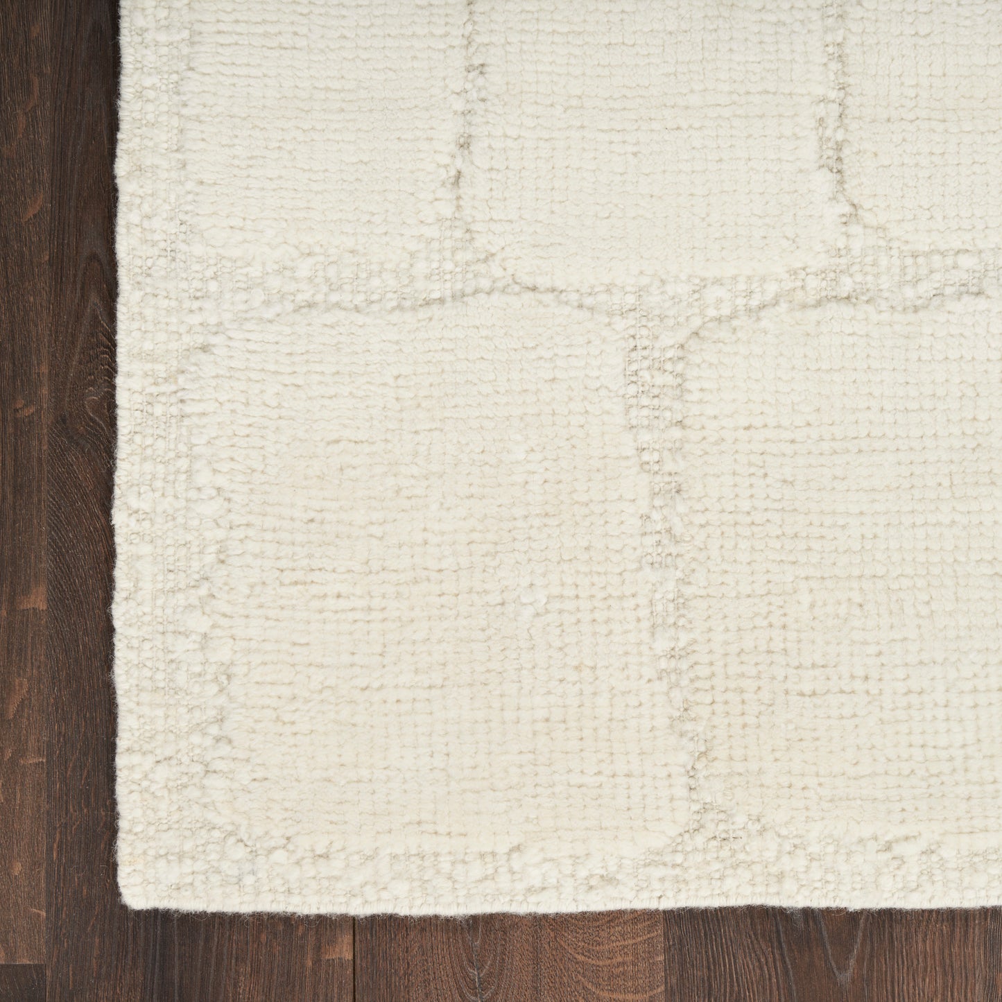 Cream textured area rug with subtle square patch pattern on dark wood floor.