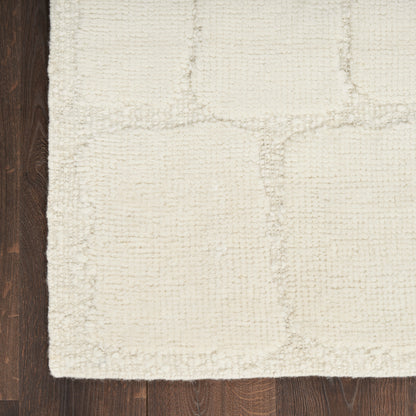 Cream textured area rug with subtle square patch pattern on dark wood floor.