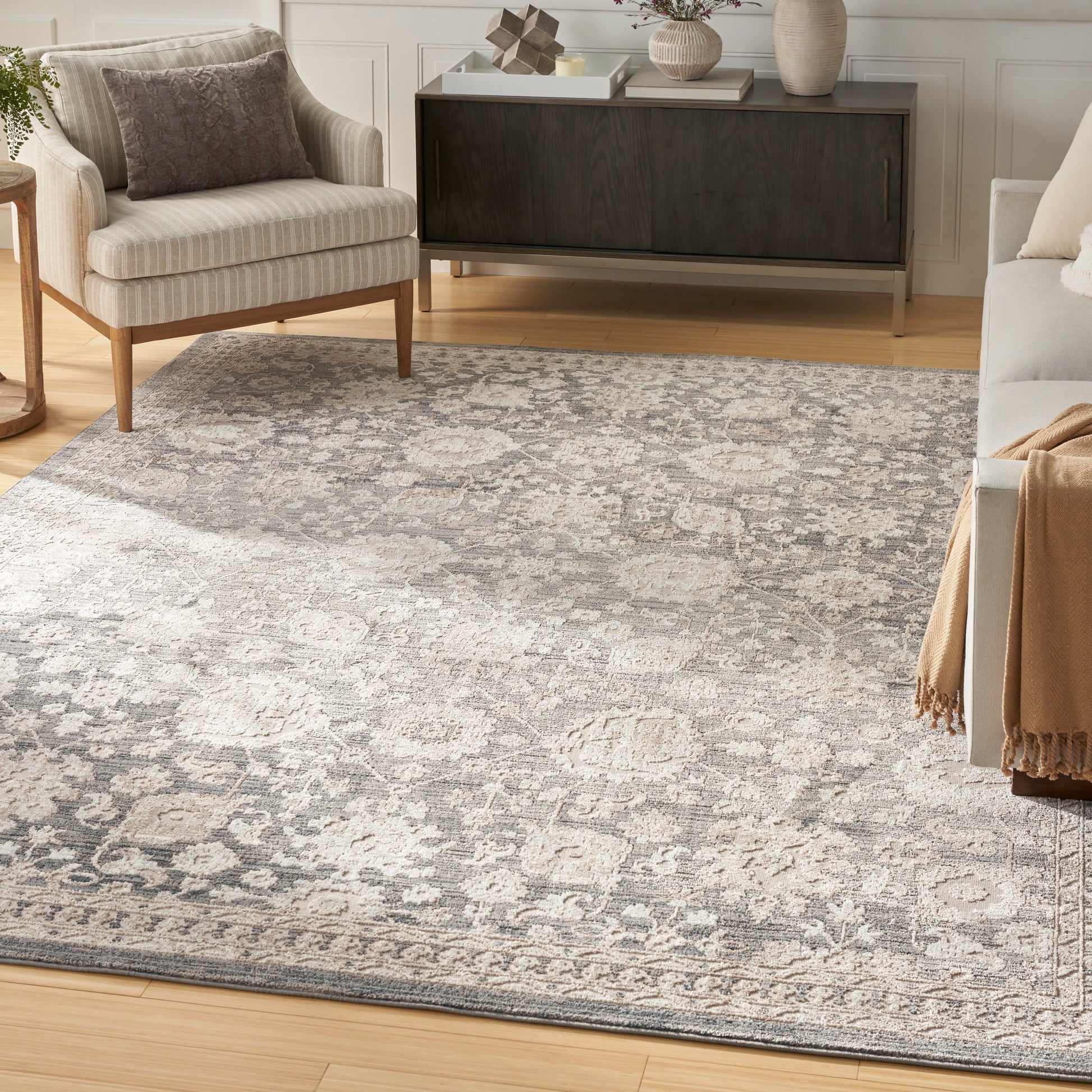Light gray patterned area rug on warm wood floor with beige armchair, gray sofa, and dark wood sideboard.