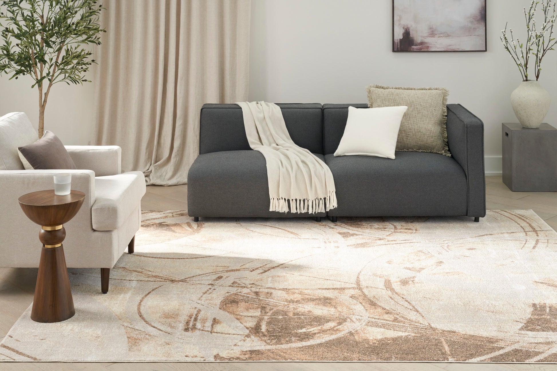Modern living room scene with a dark gray sectional sofa, cream throw, beige pillows, white armchair, and a light patterned area rug sized 7' x 9'.