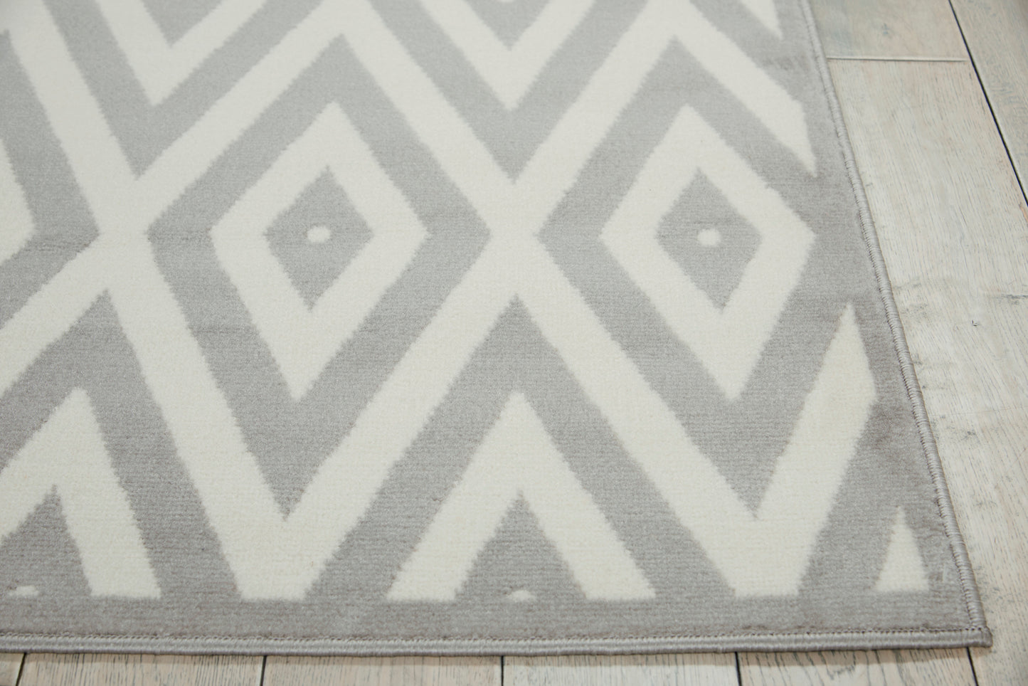 Gray and white geometric chevron rug, low-pile, rectangular, on light wood floor; modern decor.