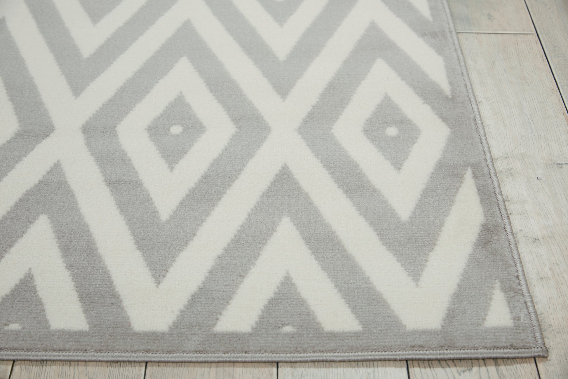 Gray and white geometric chevron rug, low-pile, rectangular, on light wood floor; modern decor.