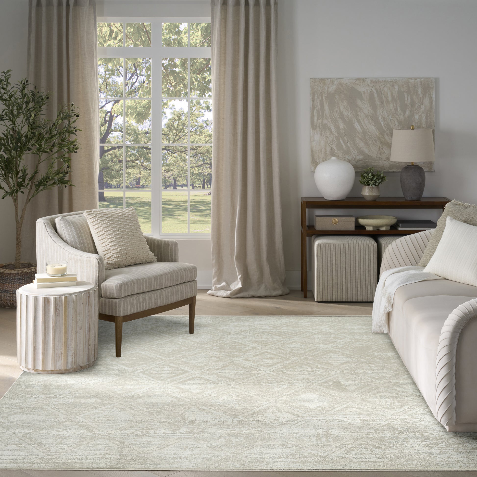 Neutral living room with beige fabric sofa and armchair, light textured rug, wooden furniture, and large window with beige curtains.