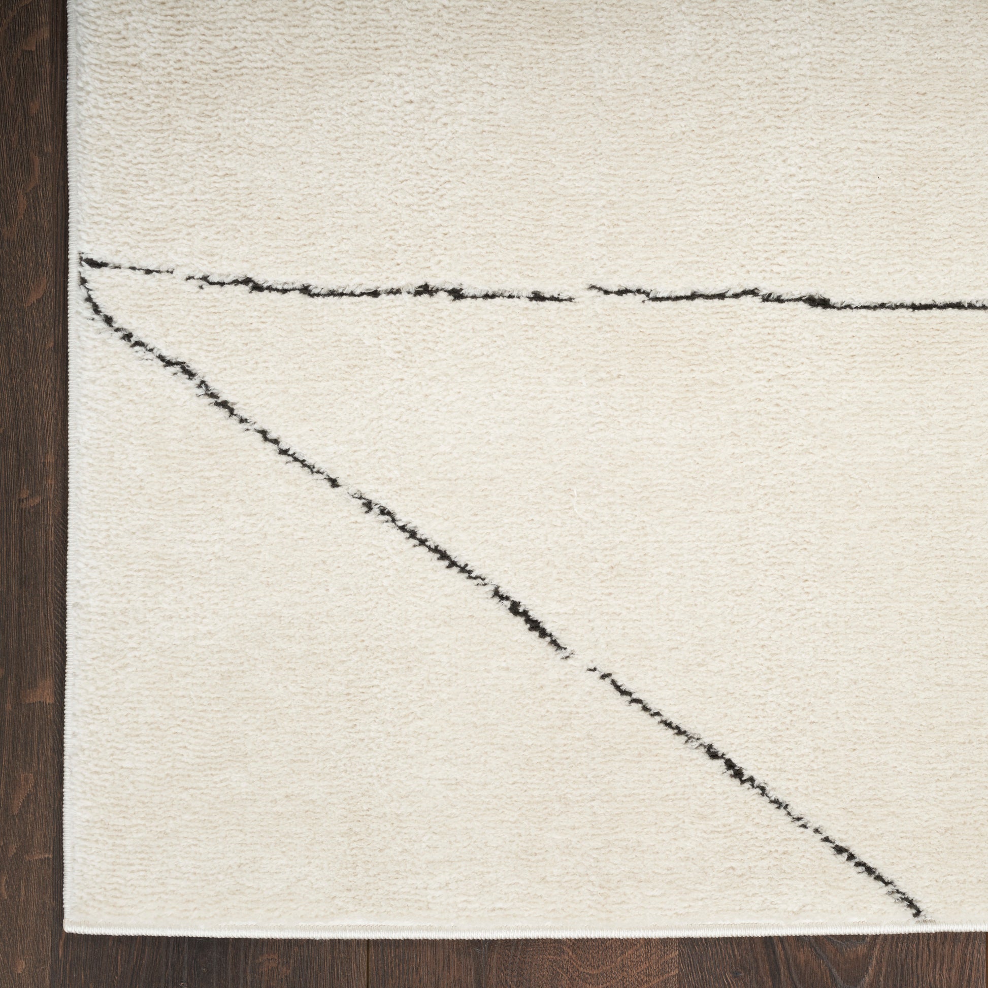 Cream shag rug with black abstract lines forming a diagonal and a horizontal stroke on dark wood floor.