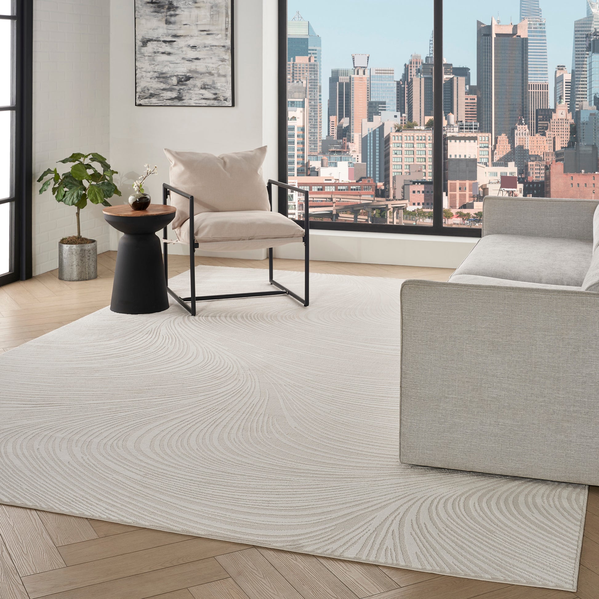 Modern living room: beige armchair with black metal frame, black wood-top side table, potted plant, cream swirl rug, city skyline view.