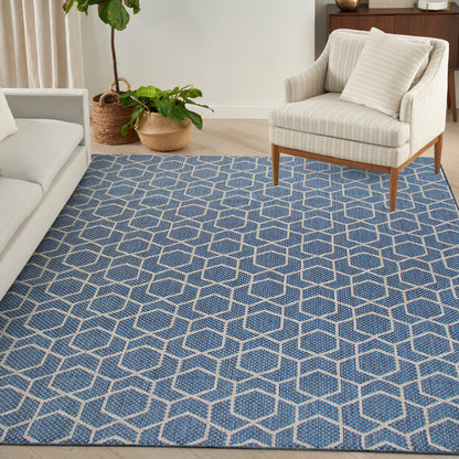 Blue geometric hexagon rug in a bright living room with a beige striped chair, light sofa, and wicker planters.