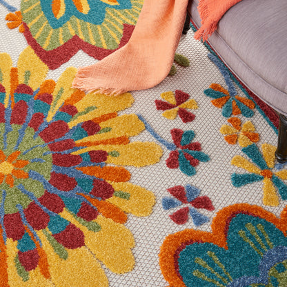 Bright multicolor floral woven rug with orange, yellow, teal petals; peach throw blanket draped over a gray sofa corner.