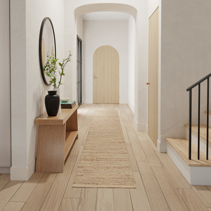 Minimalist hallway with light wood floors, beige rug runner, round wall mirror, wooden console with vase, arched doorway and stairs.