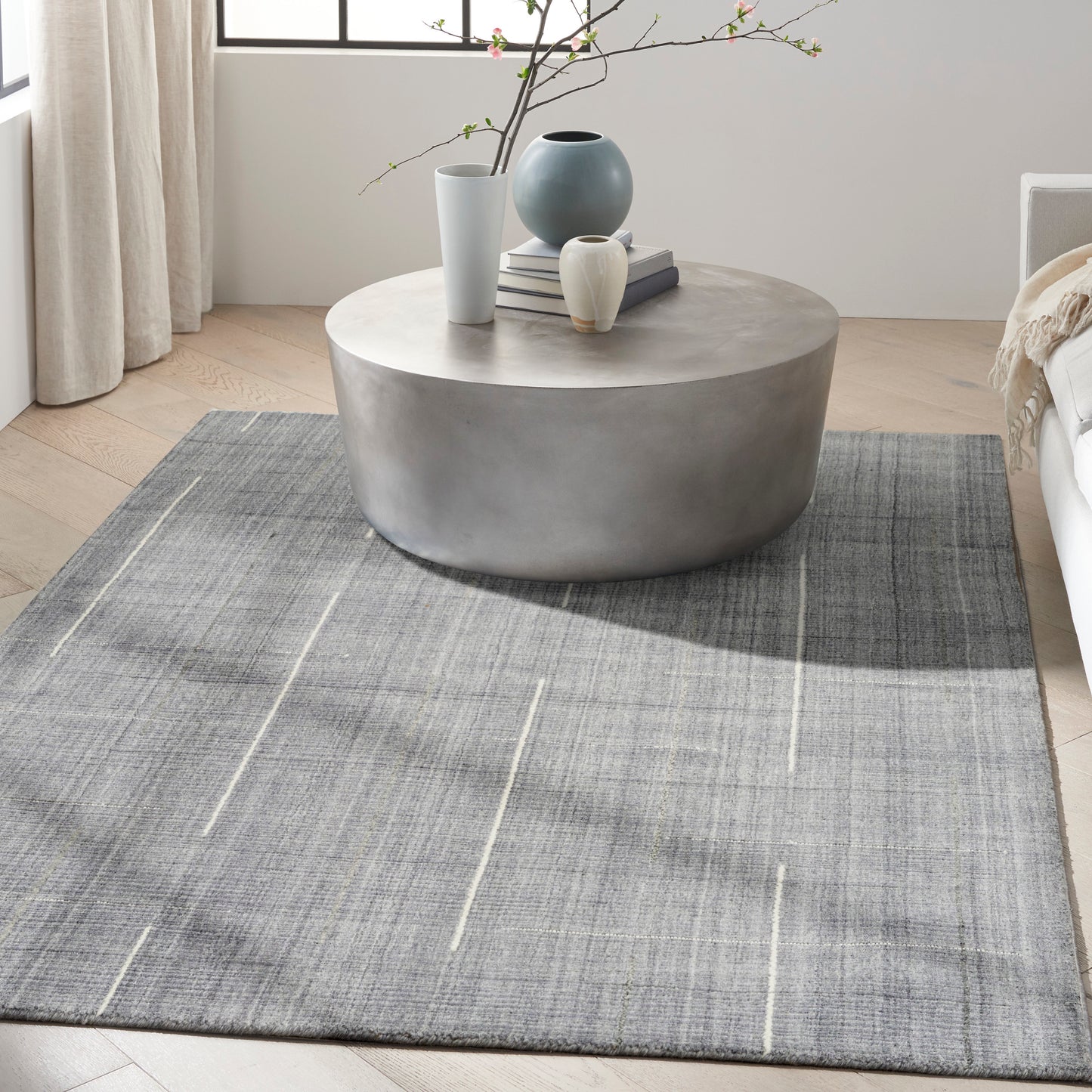 Gray striped rug on the floor in a bright modern living room with a coffee table, vases and books.