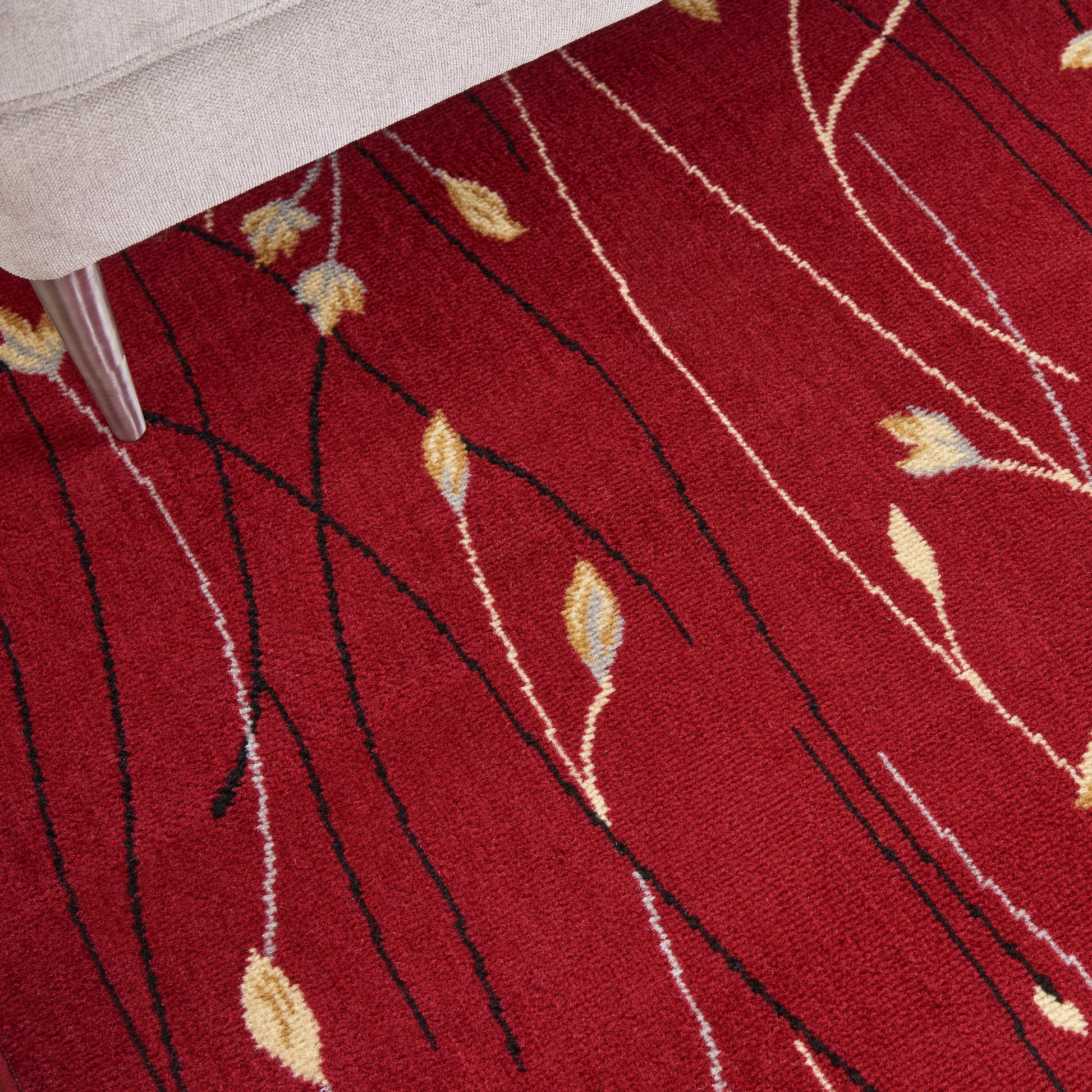 Red area rug with black wavy lines and beige leaf motifs; modern abstract pattern beside a beige sofa.