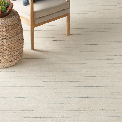 Beige rug with subtle dark flecks under a mid-century wooden-armchair and round woven rattan side table.