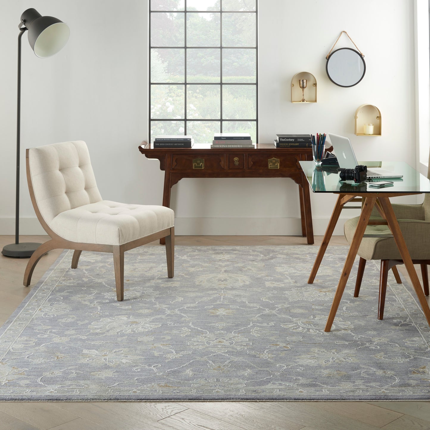 Cream tufted lounge chair with curved wood legs, glass desk, vintage sideboard, gray rug for home office.