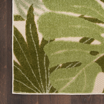 Green tropical leaf outdoor rug with olive and dark-green leaves on a beige woven background.