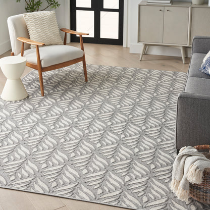 Grey and white leaf-pattern rug anchors a modern living room with a wooden armchair, round side table, and gray sofa.