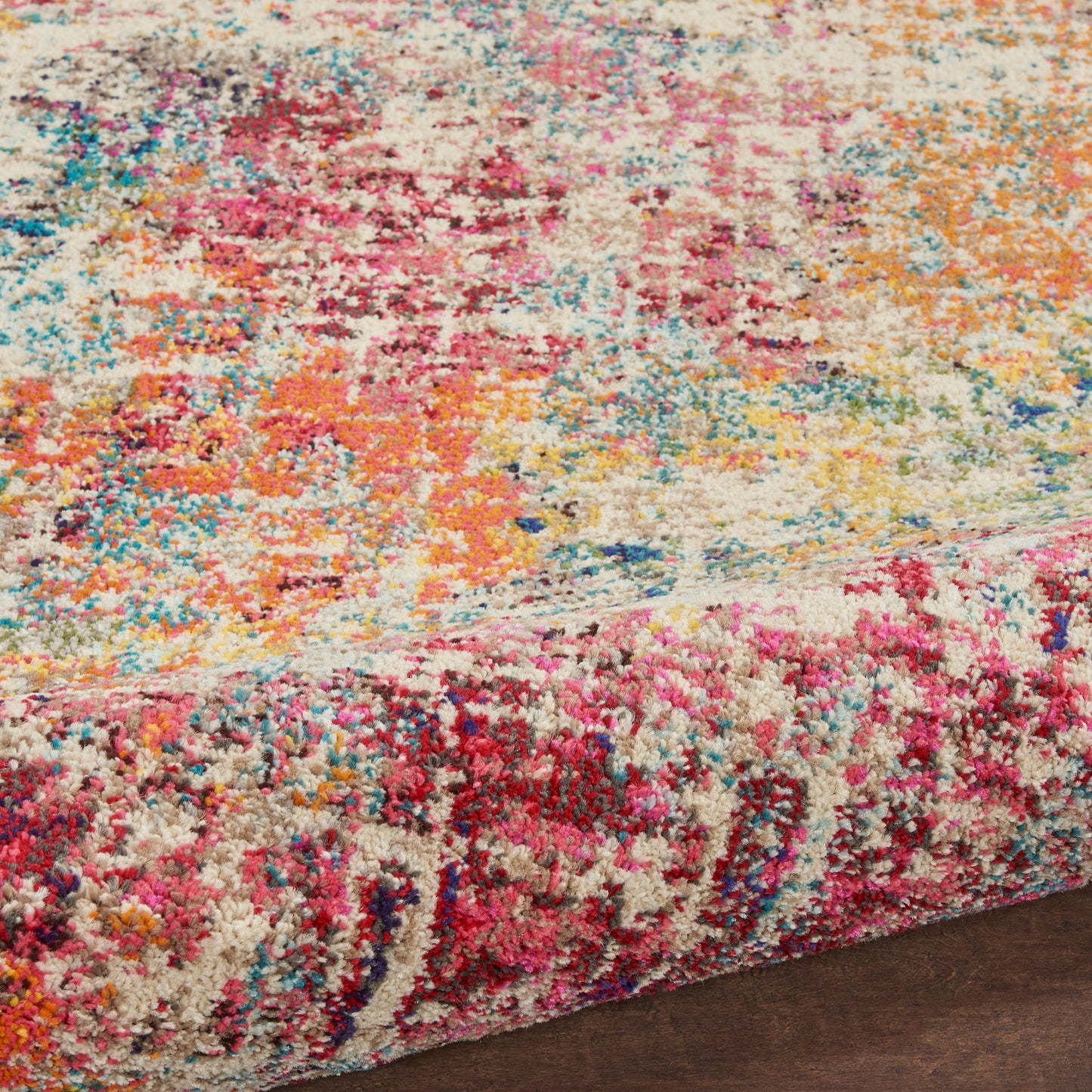 Colorful shaggy area rug with abstract splashes of pink, yellow, blue, orange on cream, shown on dark hardwood floor.