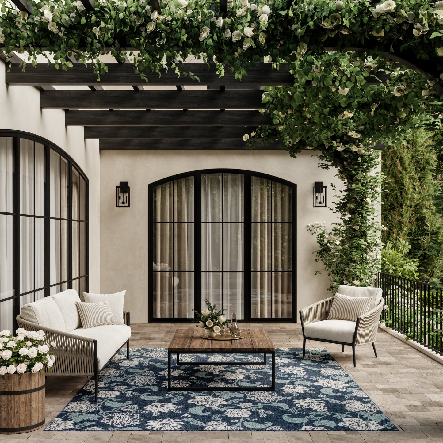 Cream cushioned seating on a sunny patio with a blue floral outdoor rug and black-framed glass doors, greenery overhead.