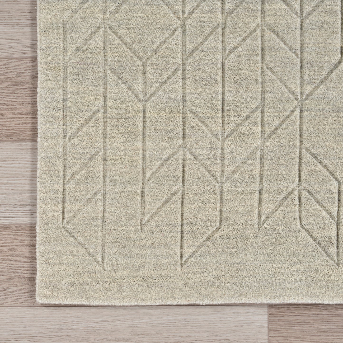 Beige flat-weave area rug with taupe geometric chevron pattern on wood floor.