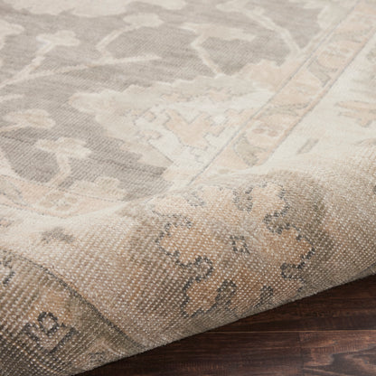 Neutral woven rectangular area rug in beige and gray with a floral medallion pattern, folded corner on dark wood floor.